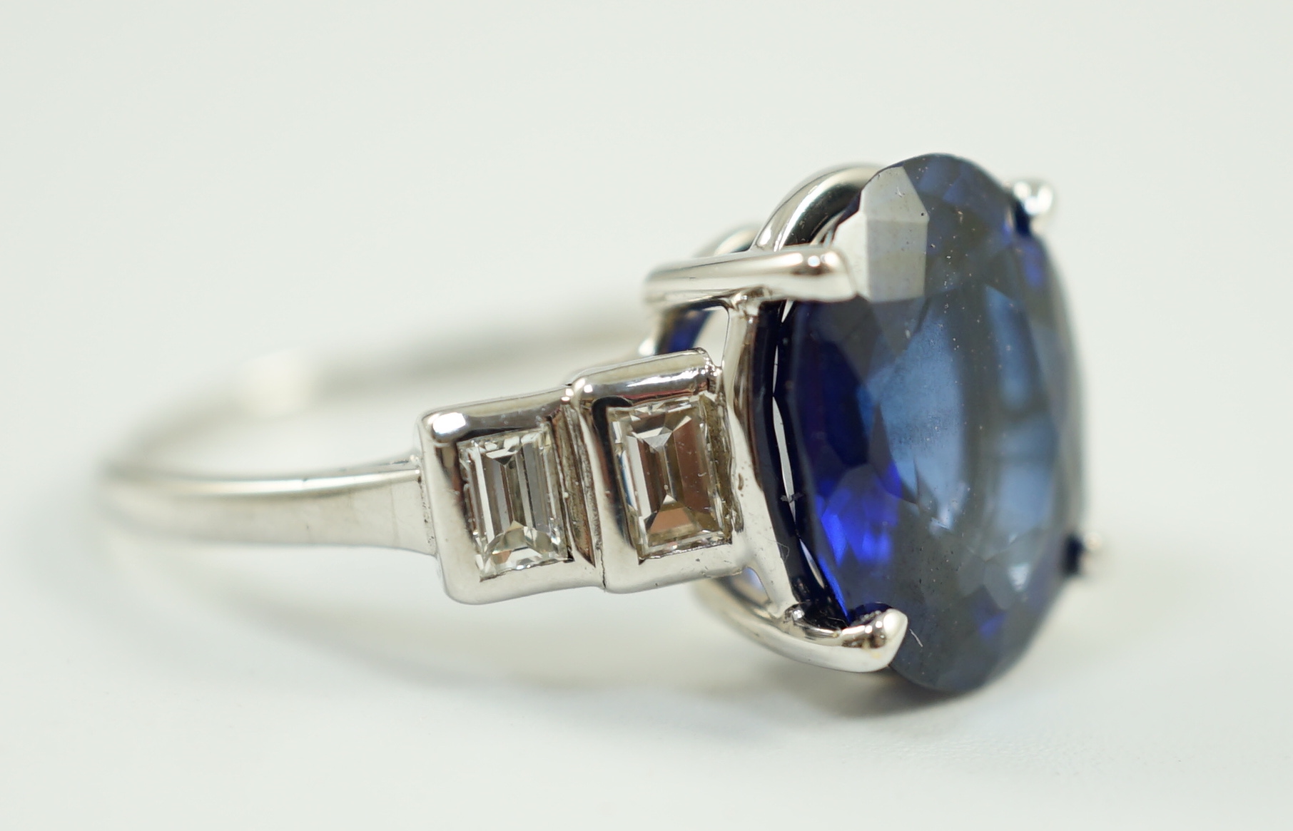 A platinum and single stone oval cut sapphire set cocktail ring, with graduated four stone baguette cut diamond set shoulders